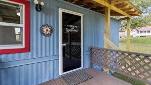 A blue building with a red-framed window, a welcome sign, and a wooden deck with a lattice railing.