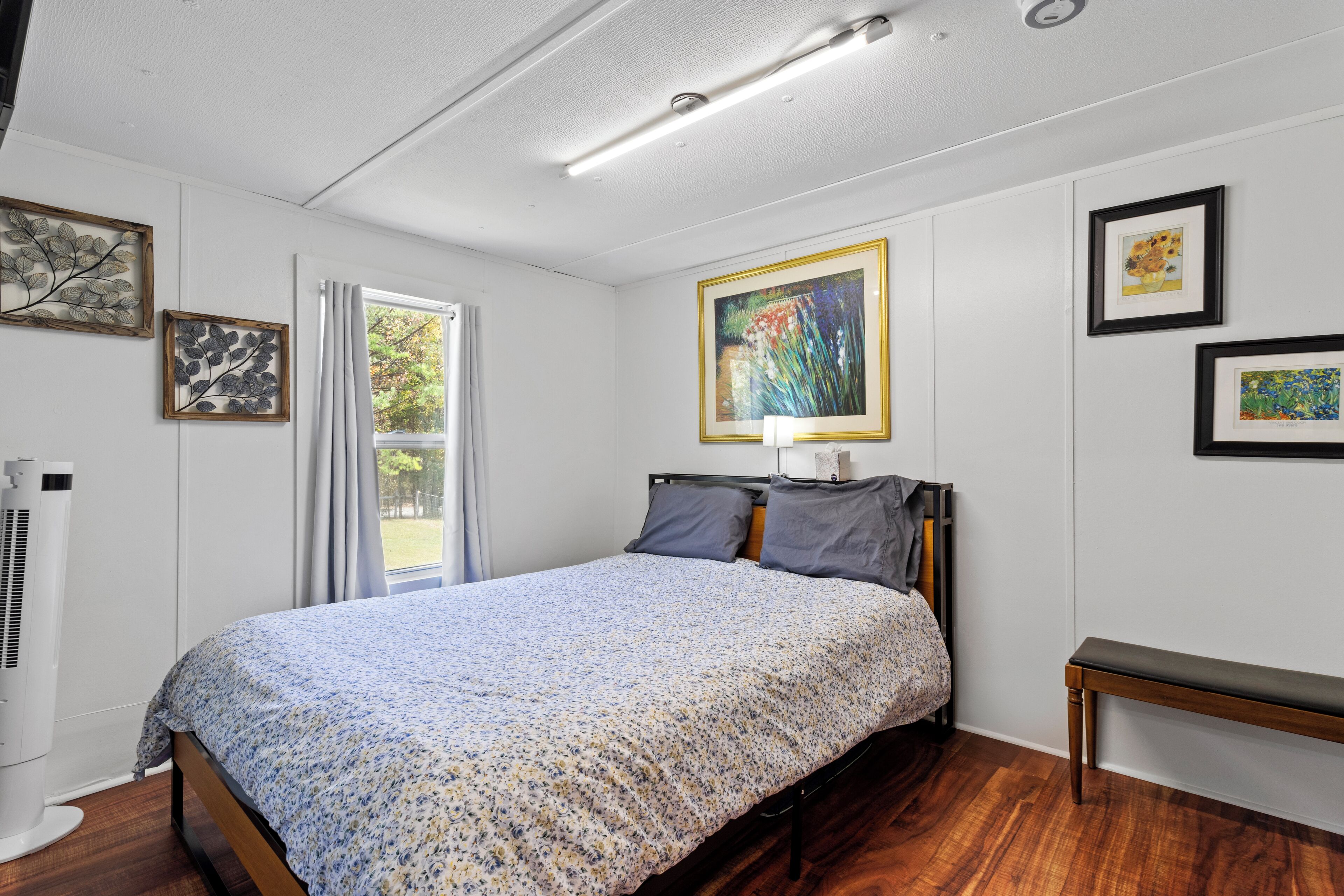 Un dormitorio con cama, mesita de noche y ventana con cortinas.