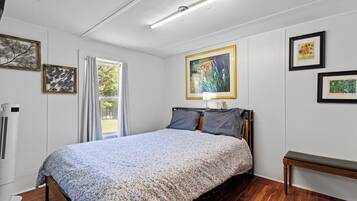 Un dormitorio con cama, mesita de noche y ventana con cortinas.