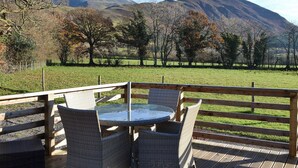 Un patio con muebles de mimbre y una mesa de vidrio, con vista a un campo cubierto de césped y montañas.