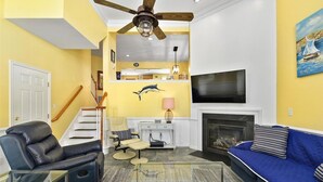 A living room with a fireplace, a TV, a sofa, a recliner, and a ceiling fan. - Large 3BR 2.5BA Garage Townhouse in Great West OC Neighborhood with Pool. (Berlin)