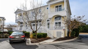 A multi-story residential building with a prominent balcony on the second floor, a driveway with a parked car, and a well-maintained lawn. - Large 3BR 2.5BA Garage Townhouse in Great West OC Neighborhood with Pool. (Berlin)