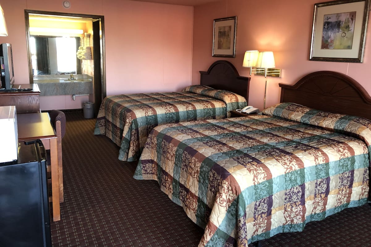 A hotel room with two beds, a desk, a mirror, and a bathroom visible through an open door.