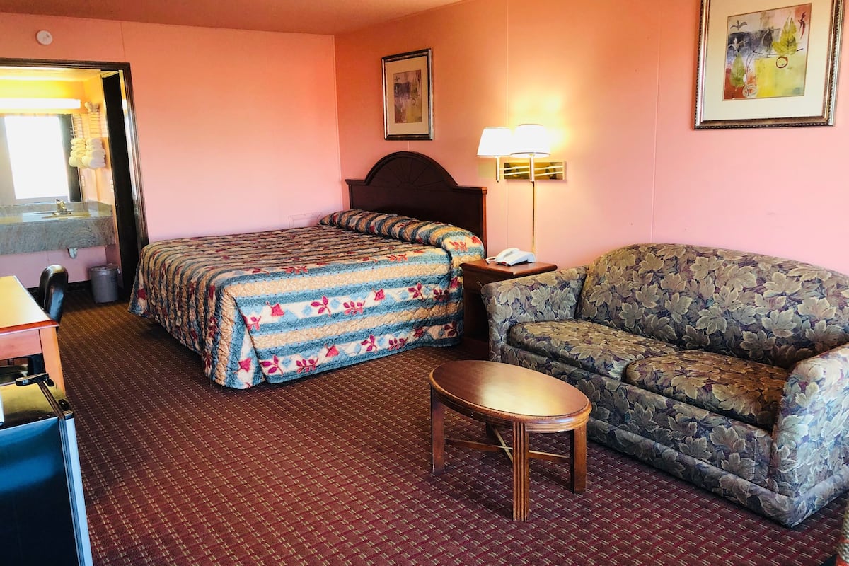 A hotel room with a bed, a sofa, a small table, a lamp, and a painting on the wall.