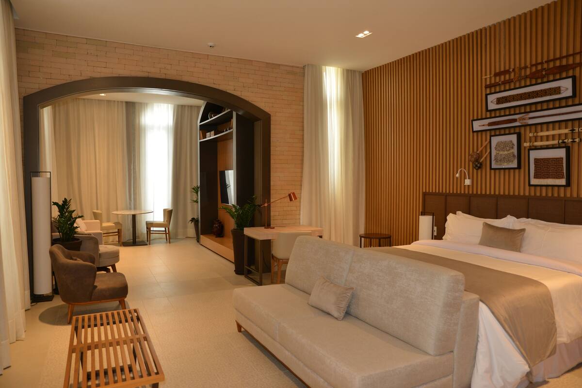 A hotel room with a bed, sofa, armchair, small table, and a mirror.