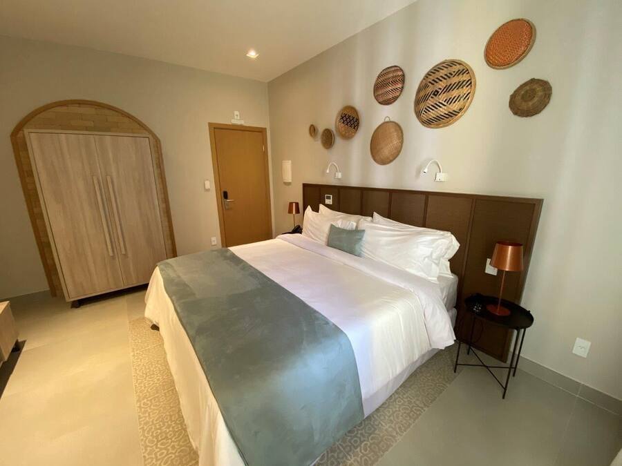 A hotel room with a large bed, a wardrobe, a bedside table with a lamp, and decorative woven baskets on the wall.