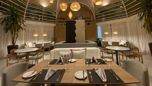 Un restaurante moderno con mesas redondas preparadas para comer, lámparas de mimbre colgantes y una escultura central.