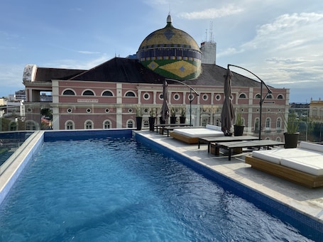 Una piscina al aire libre, sombrillas, sillones reclinables de piscina