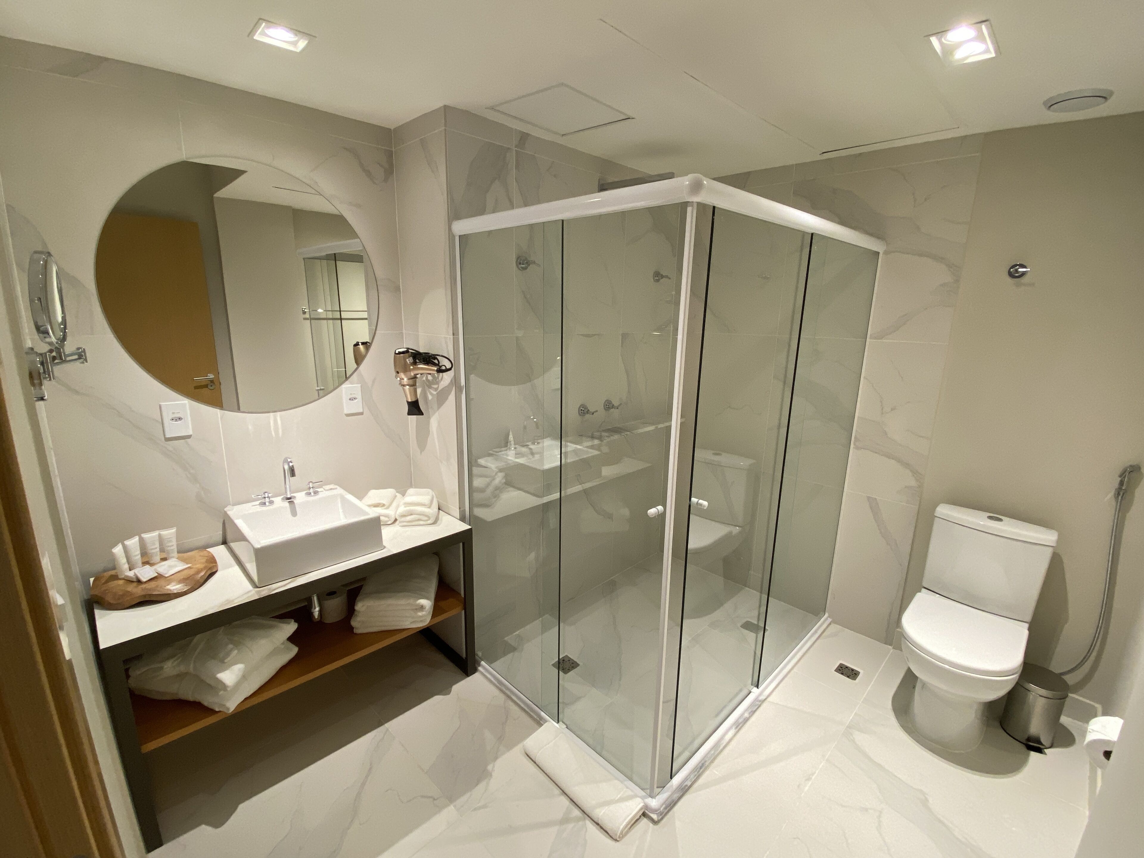 Un baño moderno con ducha envuelta en vidrio, lavamanos con espejo e inodoro.
