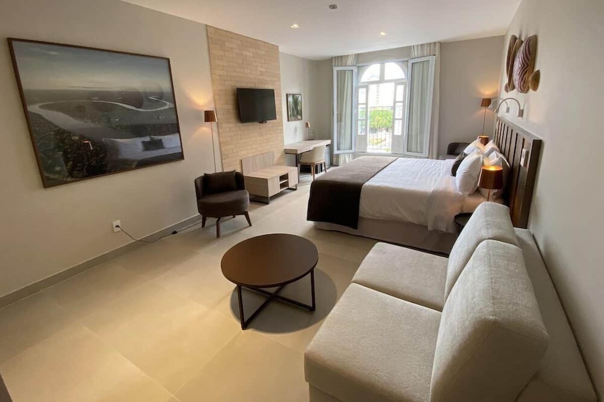 A modern hotel room with a large bed, a sofa, a desk, and a TV.