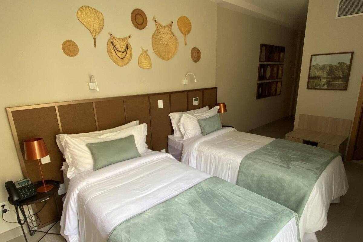 A hotel room with two beds, a bedside table with a lamp, and a wall decorated with woven hats.