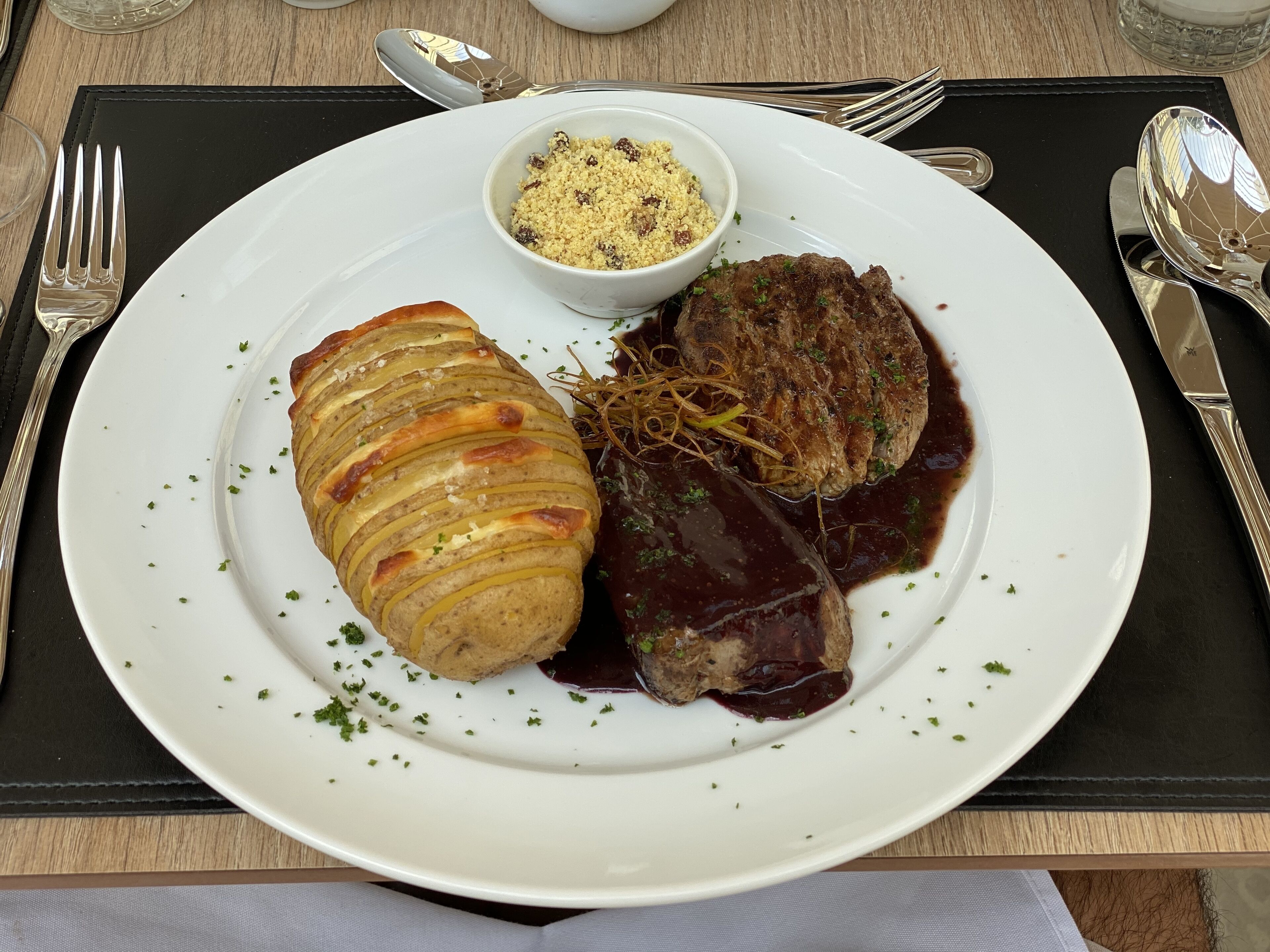Een bord met plakjes aardappel, een gehaktburger en een portie couscous.
