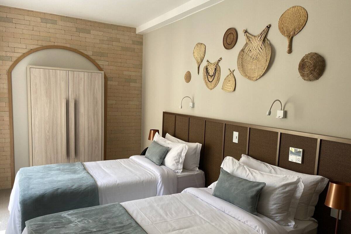 A hotel room with two beds, a brick wall, and decorative woven items on the wall.