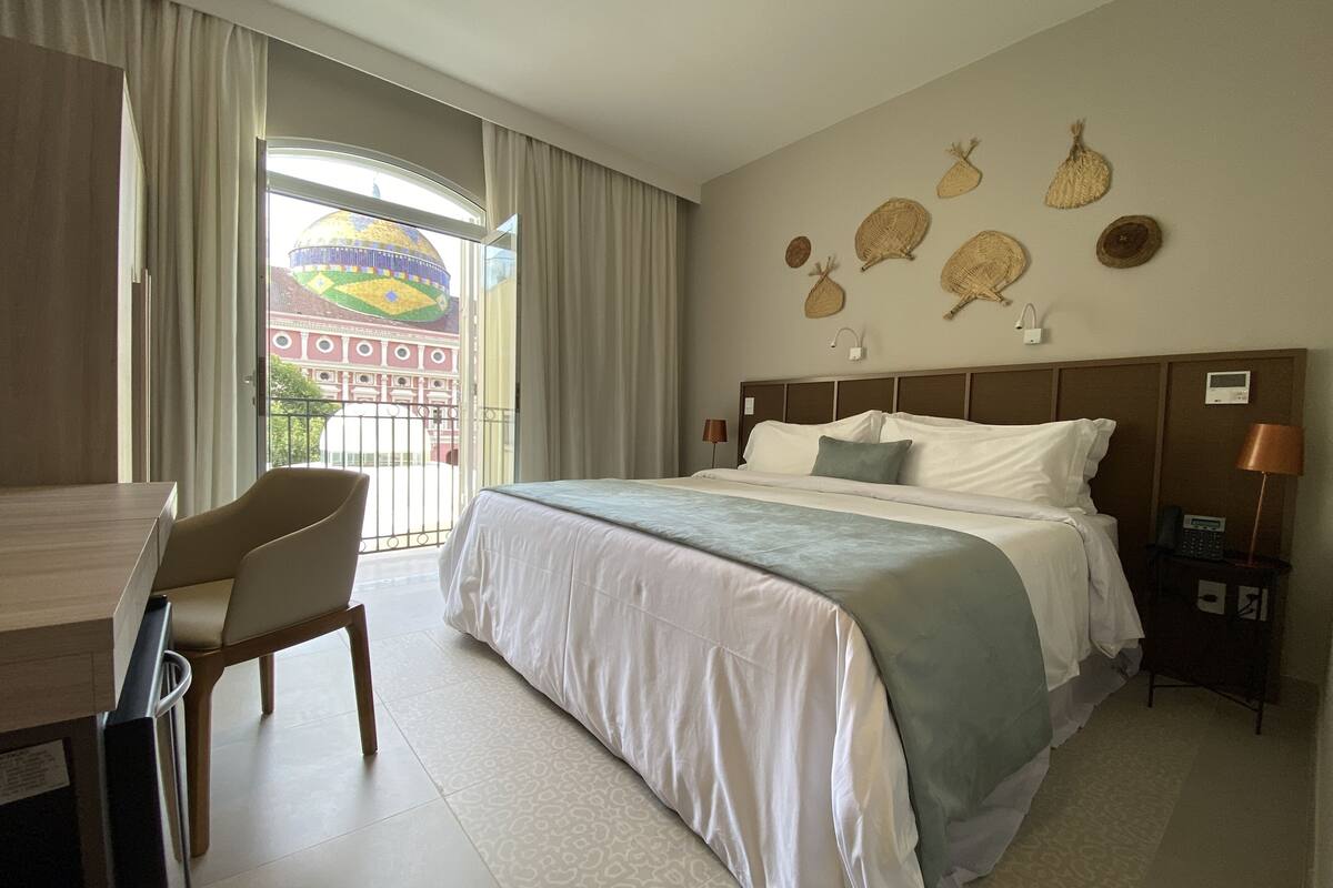 A hotel room with a bed, a desk, and a chair. There is a view of a building with a dome through the window.