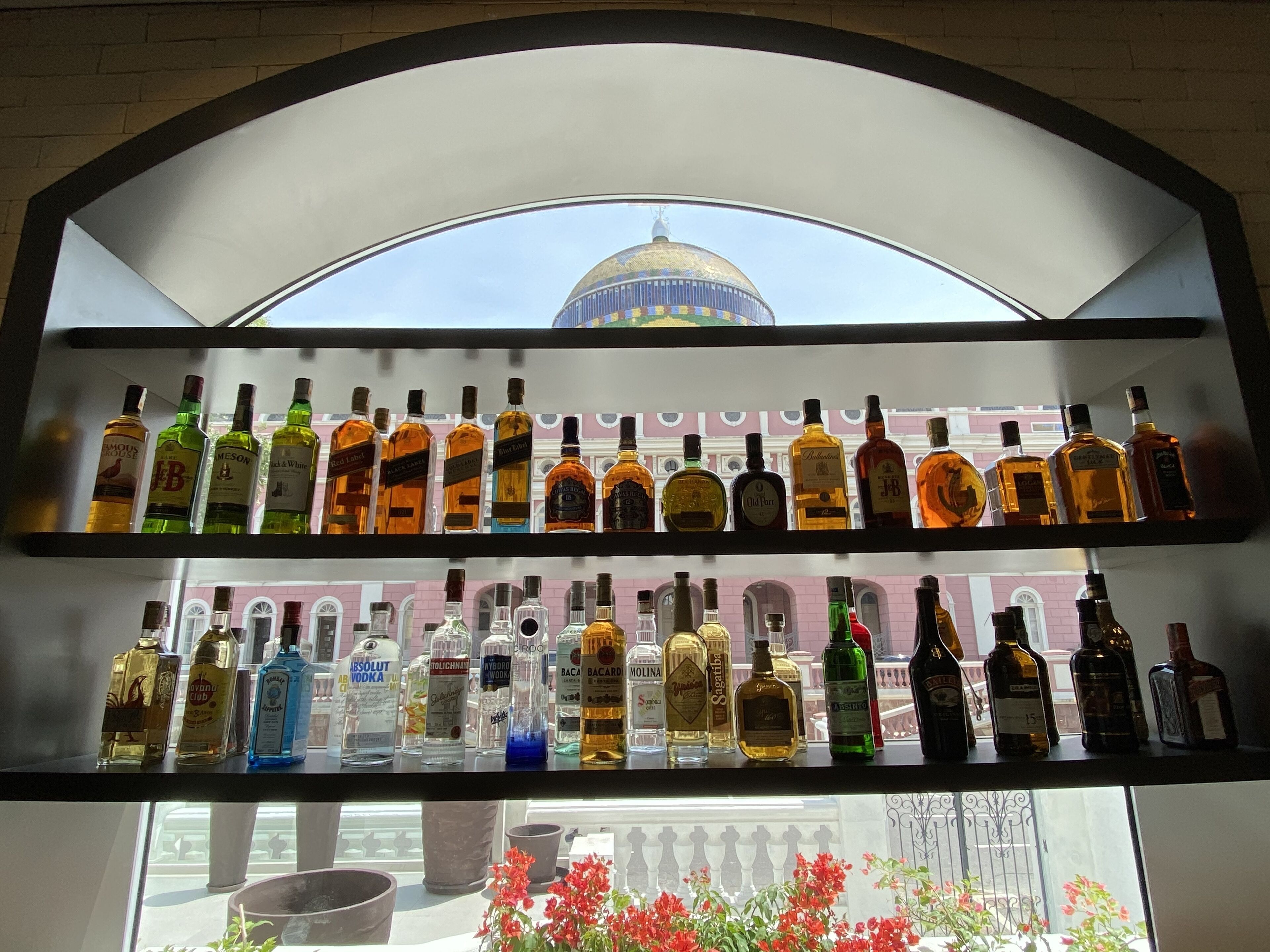 Exposição de garrafas de bebidas em uma loja, com vista para um edifício com cúpula ao fundo.