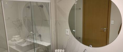 Un baño moderno con ducha envuelta en cristal, un espejo redondo y un lavamanos blanco.