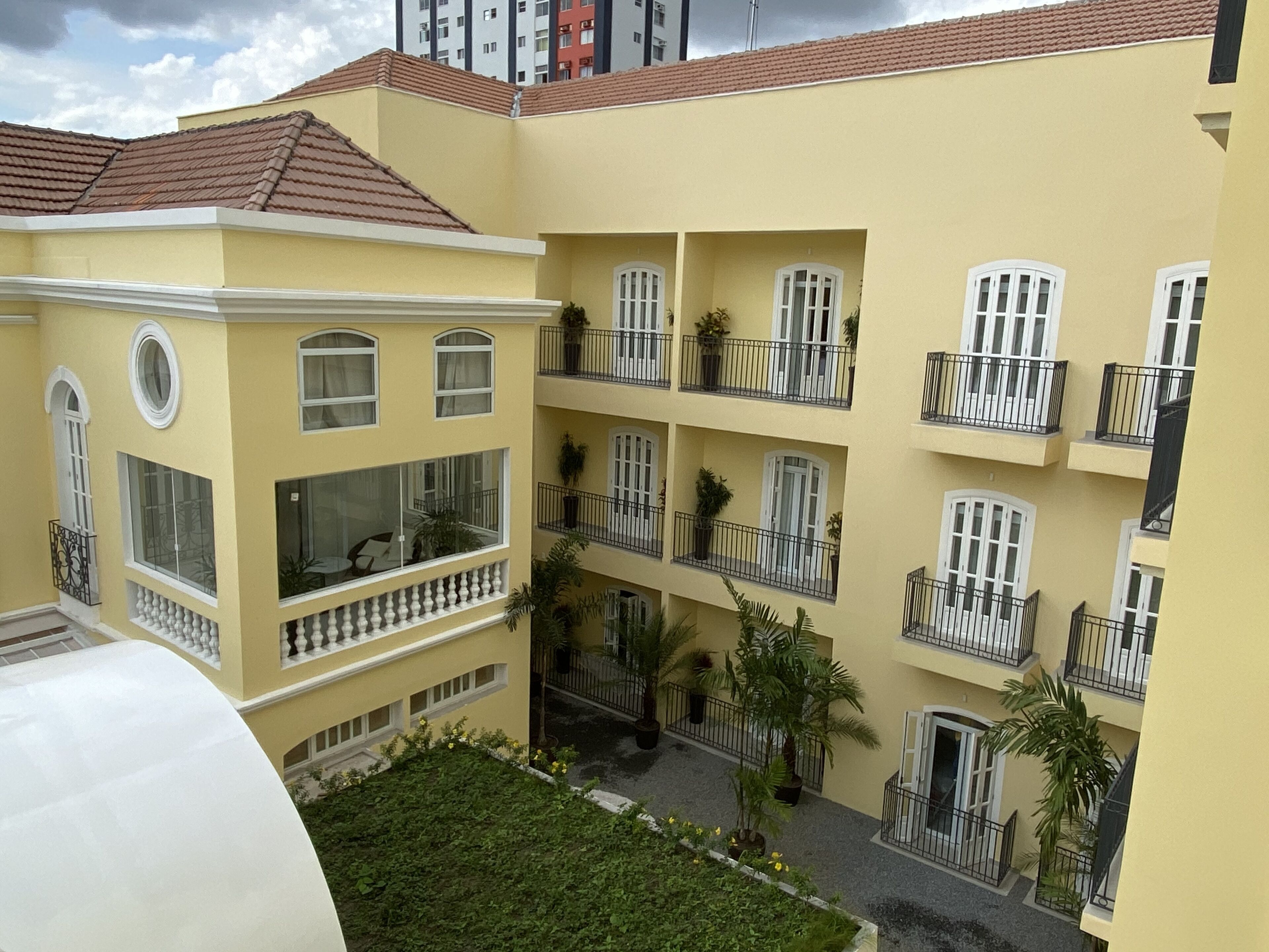 Un edificio de varios pisos con balcones, ventanas amplias y un patio con plantas.