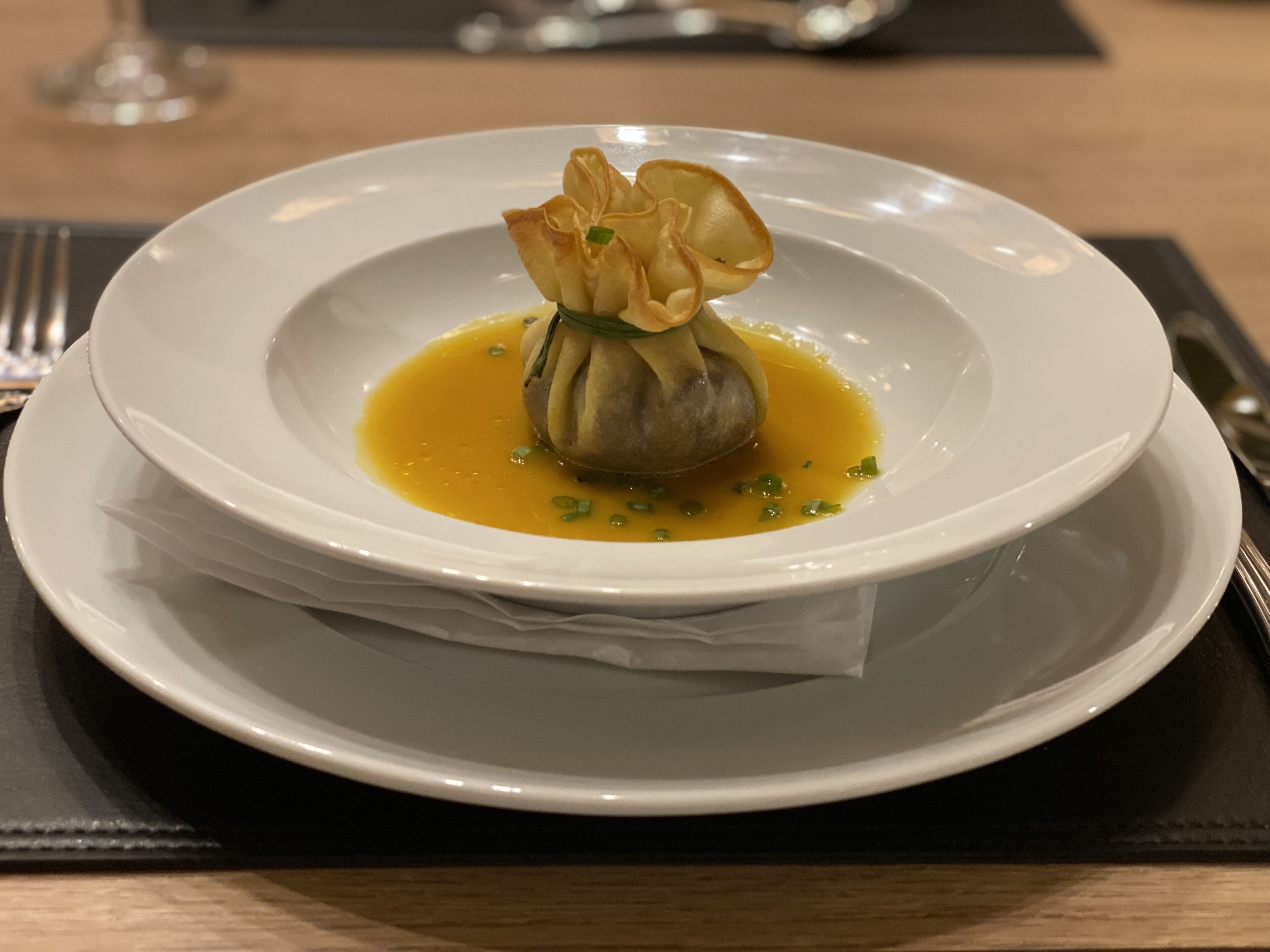 A white plate with a dumpling and sauce on a wooden table.