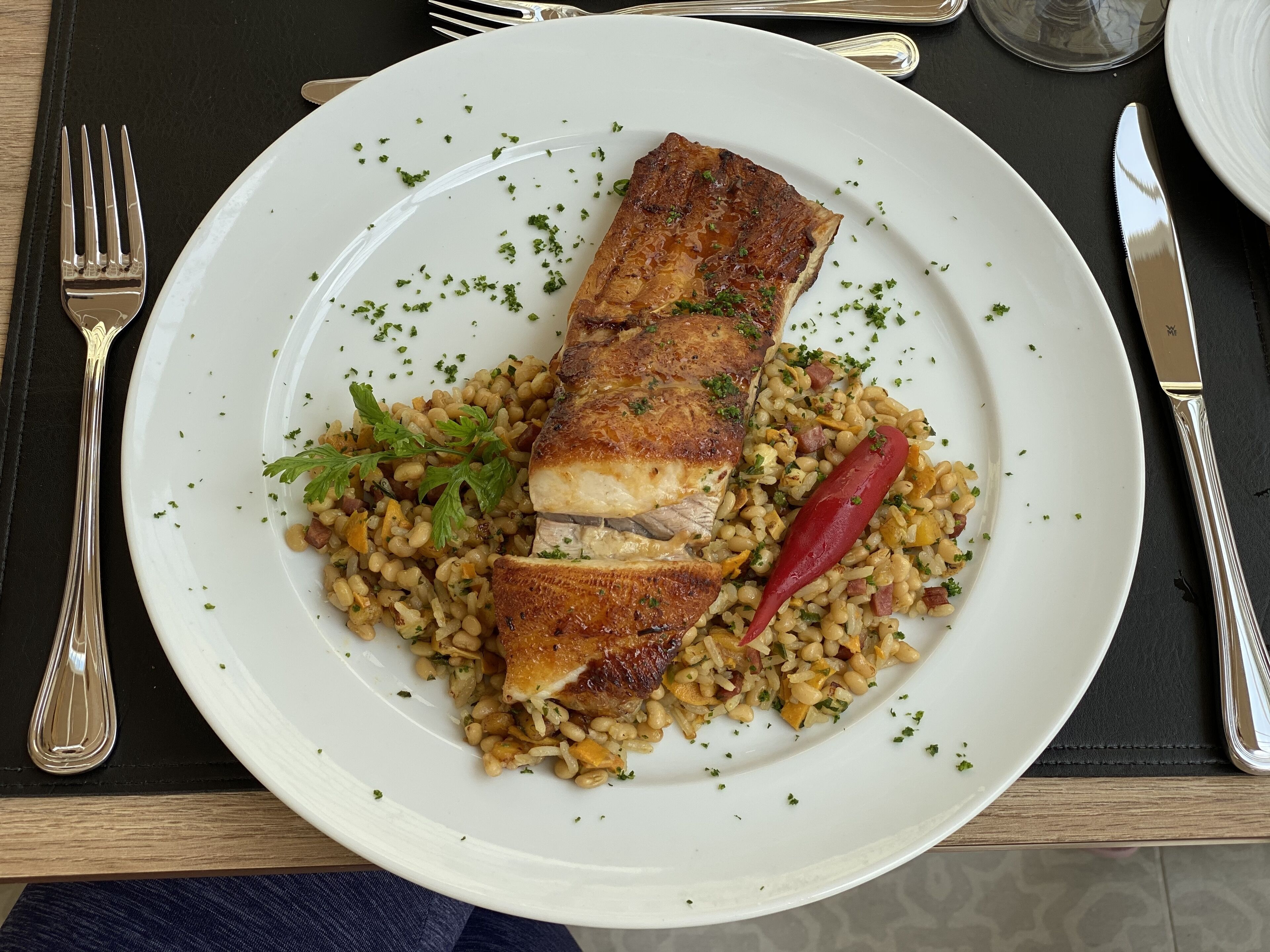 Um prato com carne assada e grãos, acompanhado de garfo e faca sobre uma mesa.