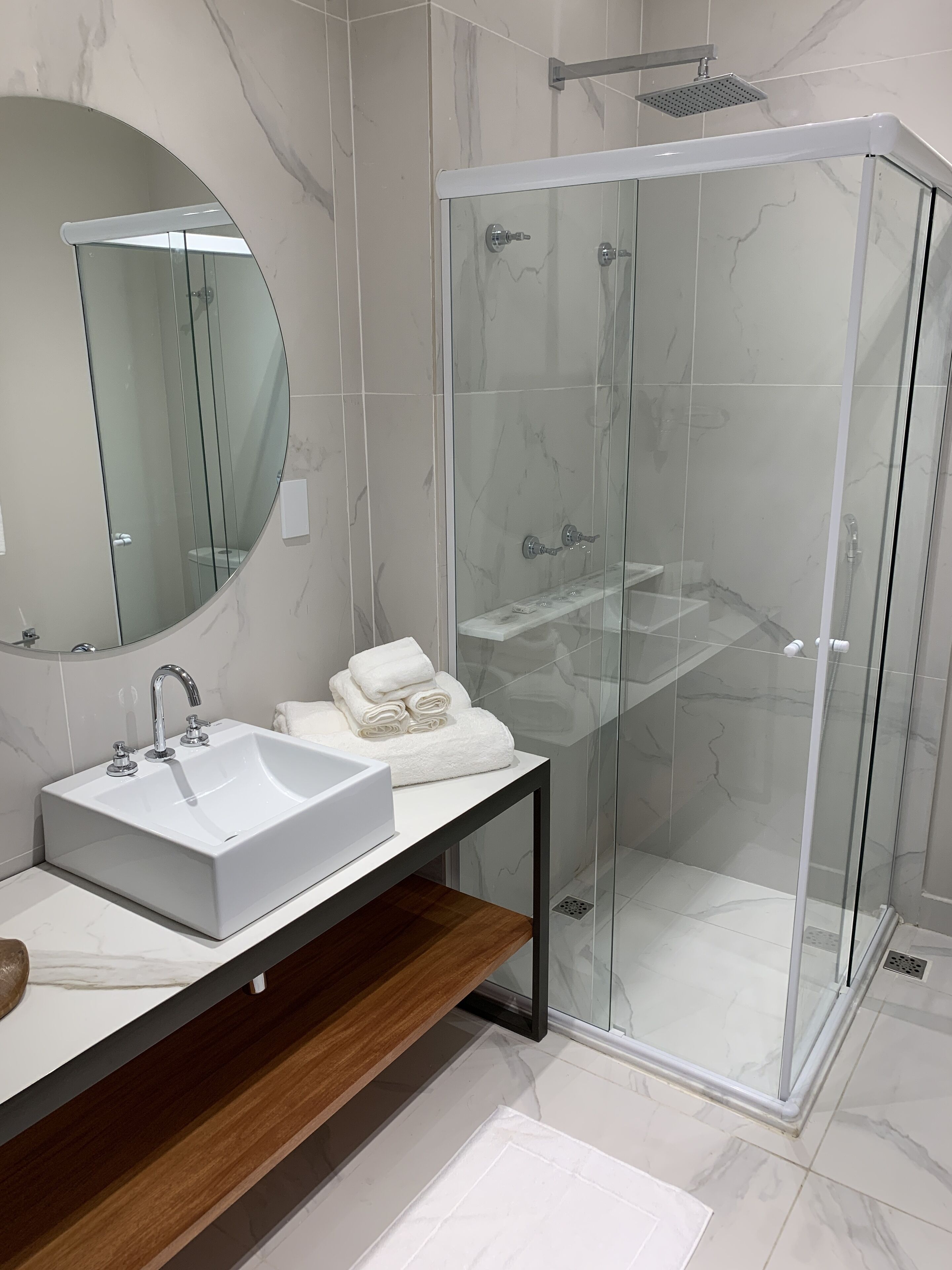 A modern bathroom with a glass-enclosed shower, a white sink, and a round mirror.