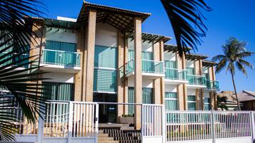 A multi-story building with balconies, a gated entrance, and palm trees.