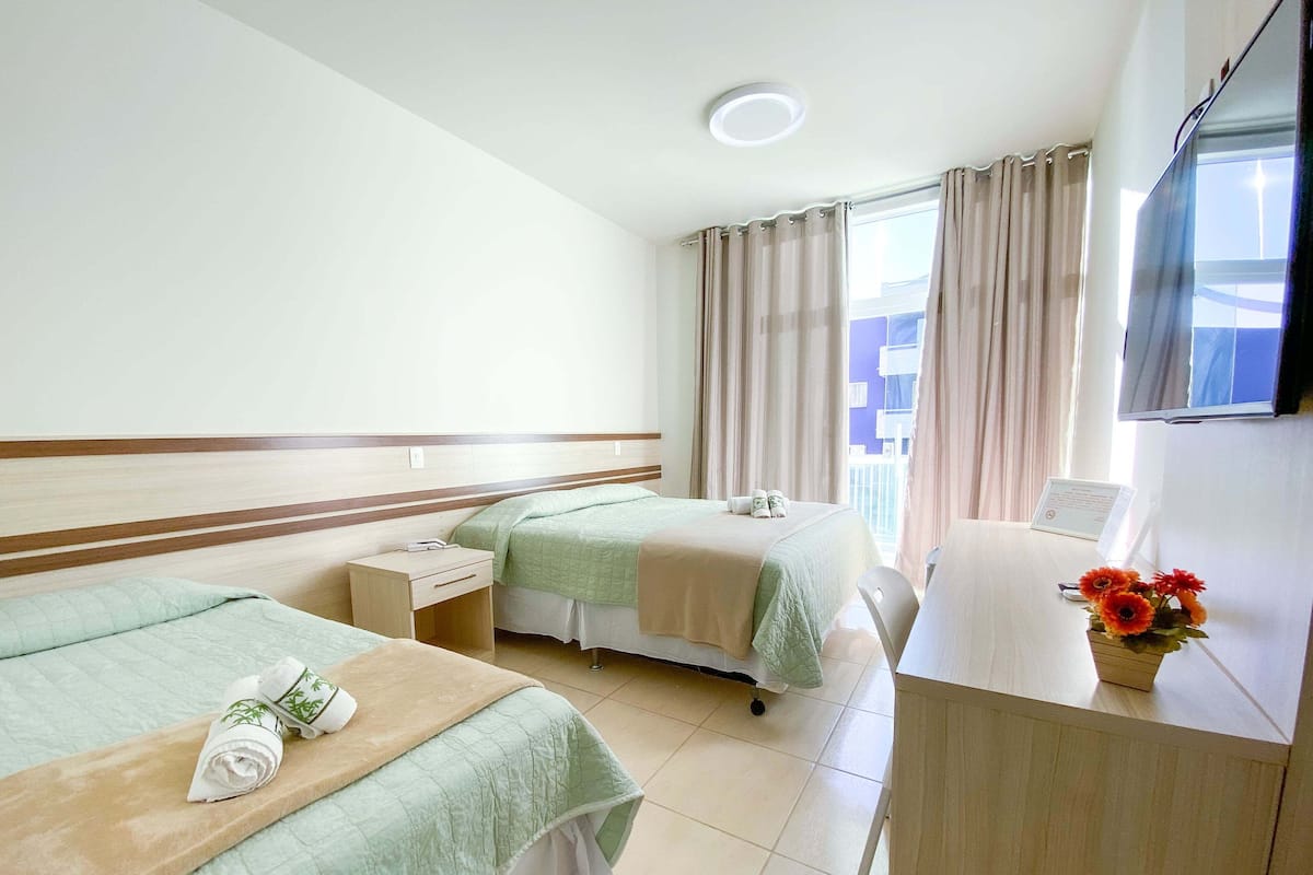 Ein Hotelzimmer mit zwei Betten, einem Schreibtisch, einem Stuhl, einem Fernseher und einem Fenster mit Vorhängen.