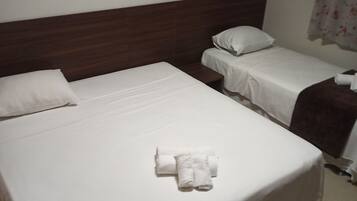 Habitación de hotel con dos camas individuales, cabecera de madera, ropa de cama blanca y una toalla enrollada sobre la cama.