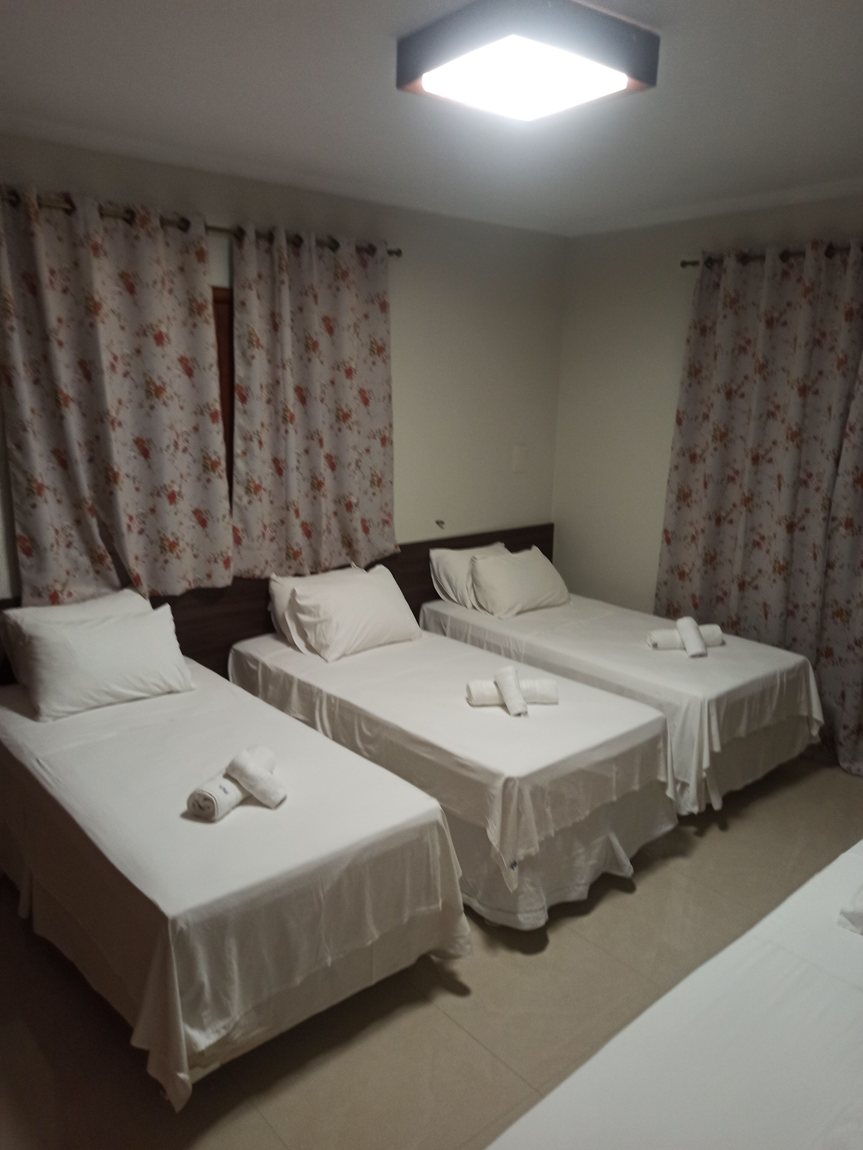 A hotel room with three single beds, each with a rolled towel and white bedding.