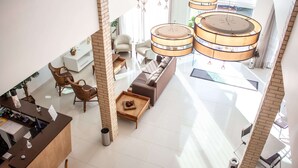 Un vestíbulo amplio con mostrador de recepción, zona de estar y un espacio abierto y diáfano con techos altos y lámparas colgantes.