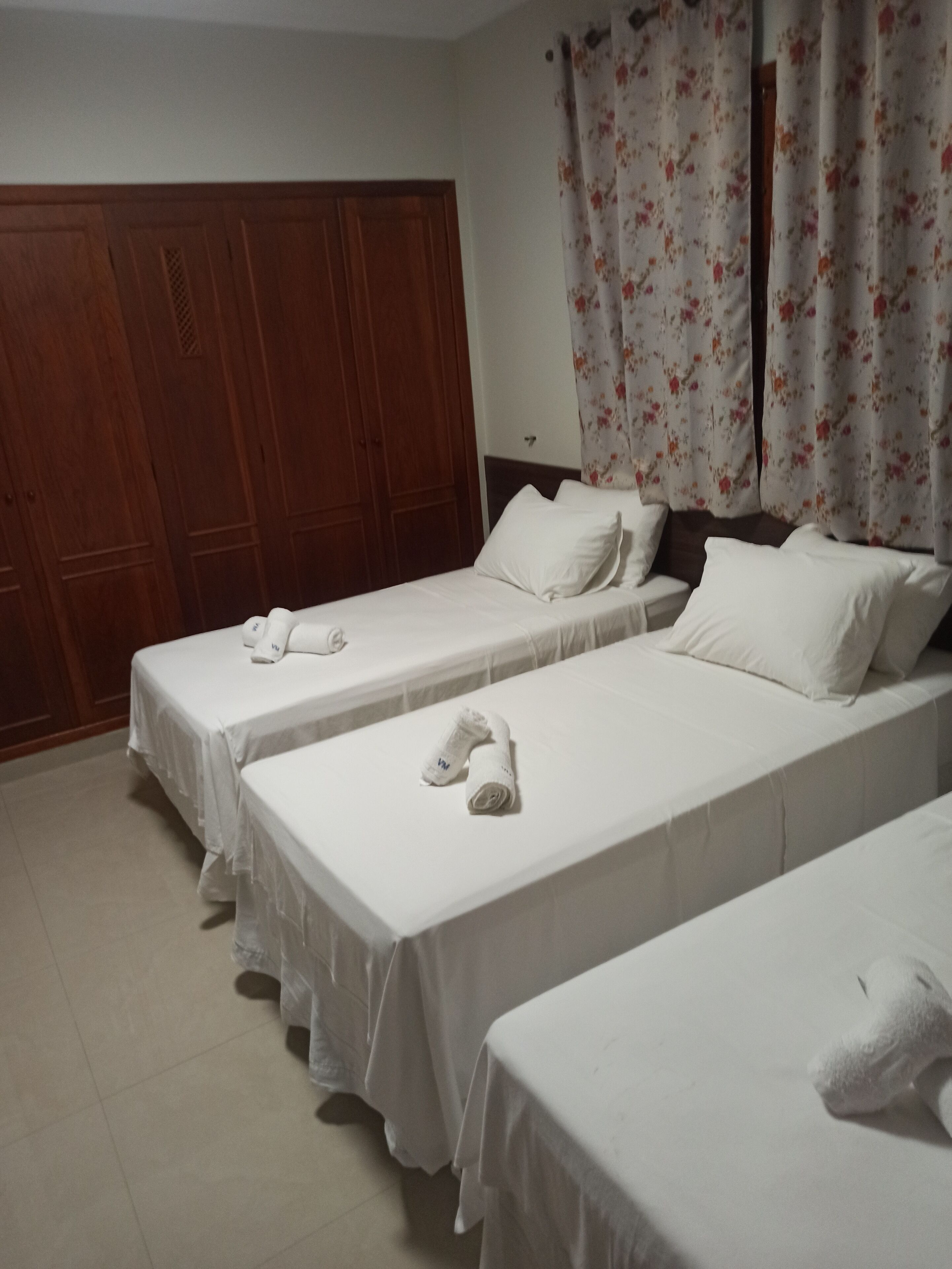 Habitación de hotel con dos camas individuales, un armario de madera y una cortina con estampado floral.