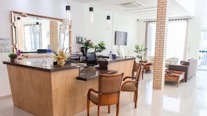 Un área de recepción moderna con un mostrador de madera, dos sillas de mimbre, un espejo grande y un televisor en la pared.