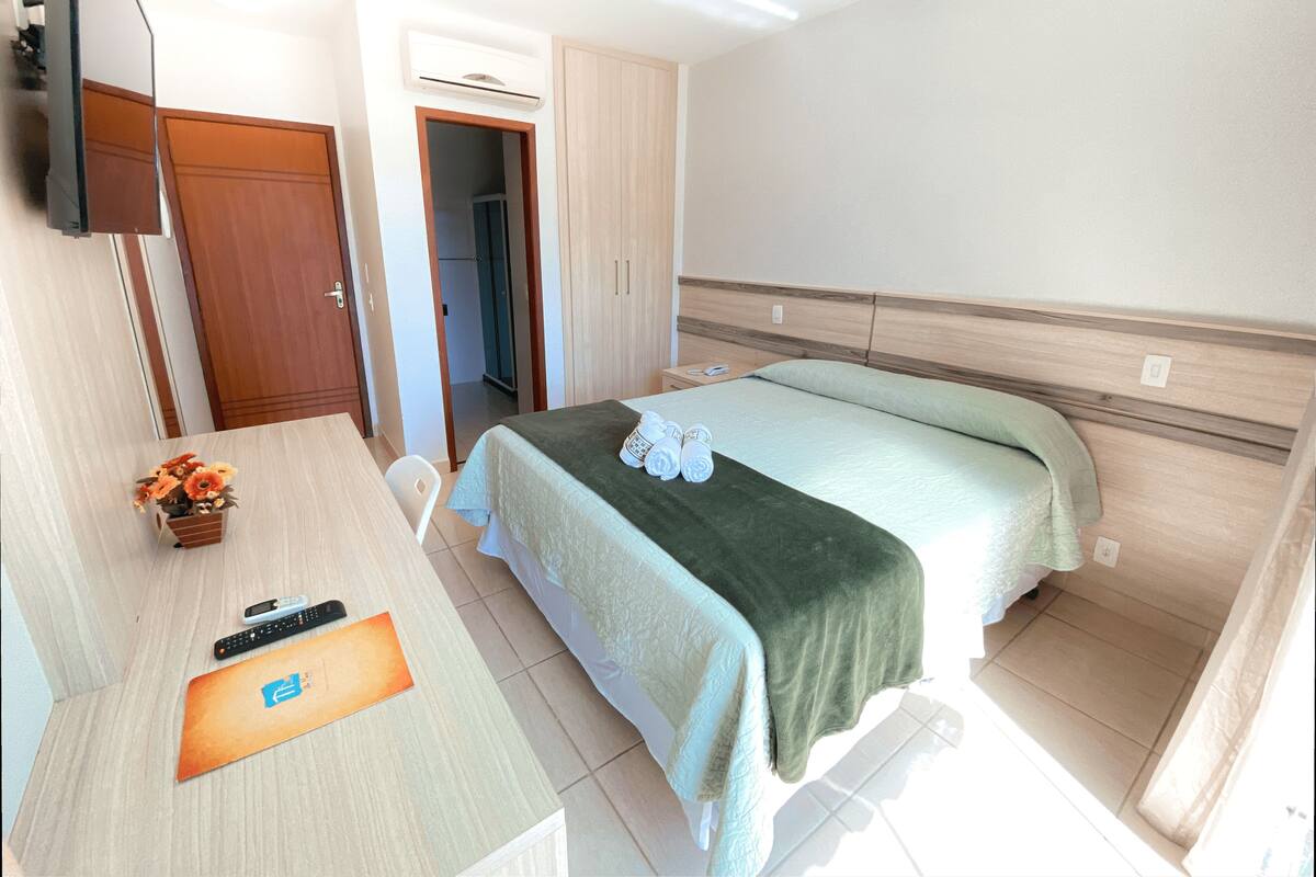 Ein Hotelzimmer mit einem Bett, einem Schreibtisch, einem Sessel, einem Fernseher und einem kleinen Tisch mit Blumen.