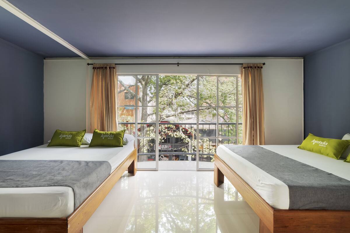 Une chambre avec deux lits, une grande fenêtre et une vue sur des arbres et un bâtiment à l’extérieur.
