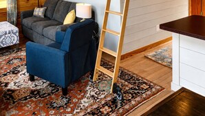 A loft-style room with a wooden ladder, a hammock, a sofa, and a dining area.