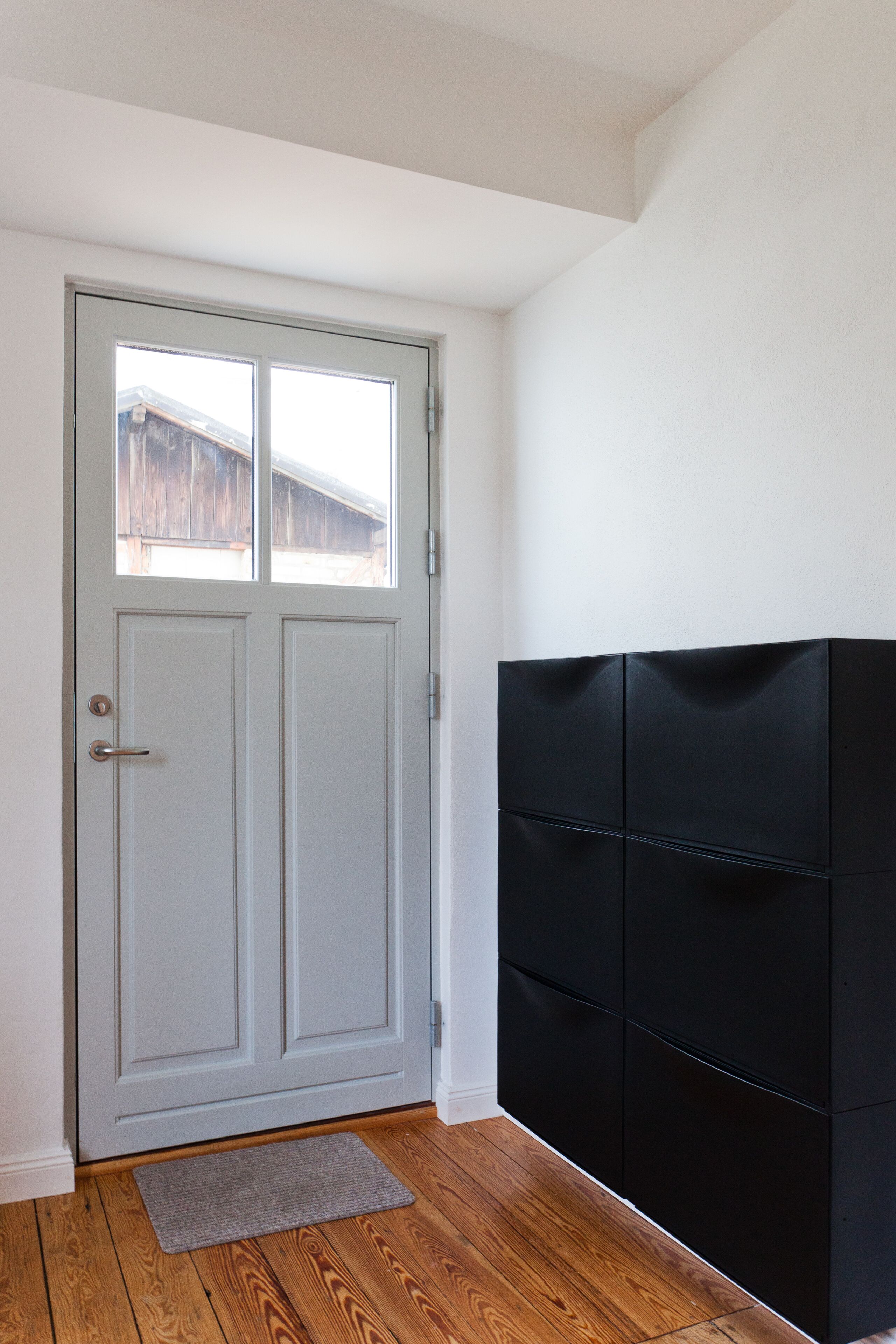 Une pièce avec une porte blanche, un meuble noir et un plancher en bois.