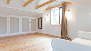 Une pièce spacieuse avec un plancher en bois, un canapé blanc et une grande fenêtre avec des rideaux.