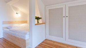 Une chambre à coucher avec un lit en bois, une table de chevet ornée d’un vase de fleurs et une armoire aux portes en verre dépoli.