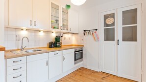 Une cuisine avec des meubles blancs, un plan de travail en bois, un évier, une cuisinière et un luminaire suspendu.