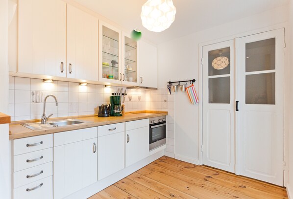 A kitchen with white cabinets, a wooden countertop, a sink, a stove, and a hanging light fixture. - Villa Luna (Sassnitz)