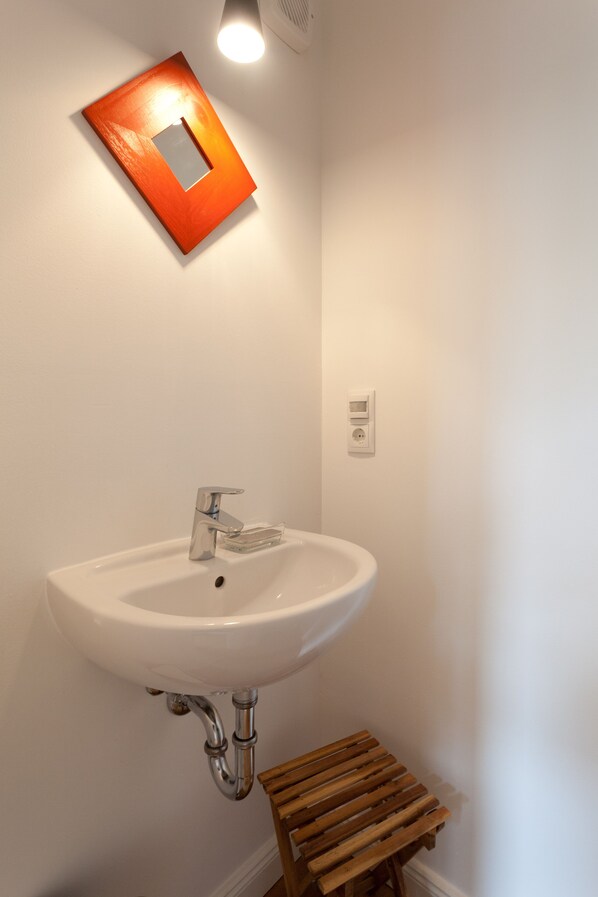 Une salle de bain avec un lavabo blanc, un robinet chromé et un tabouret en bois.