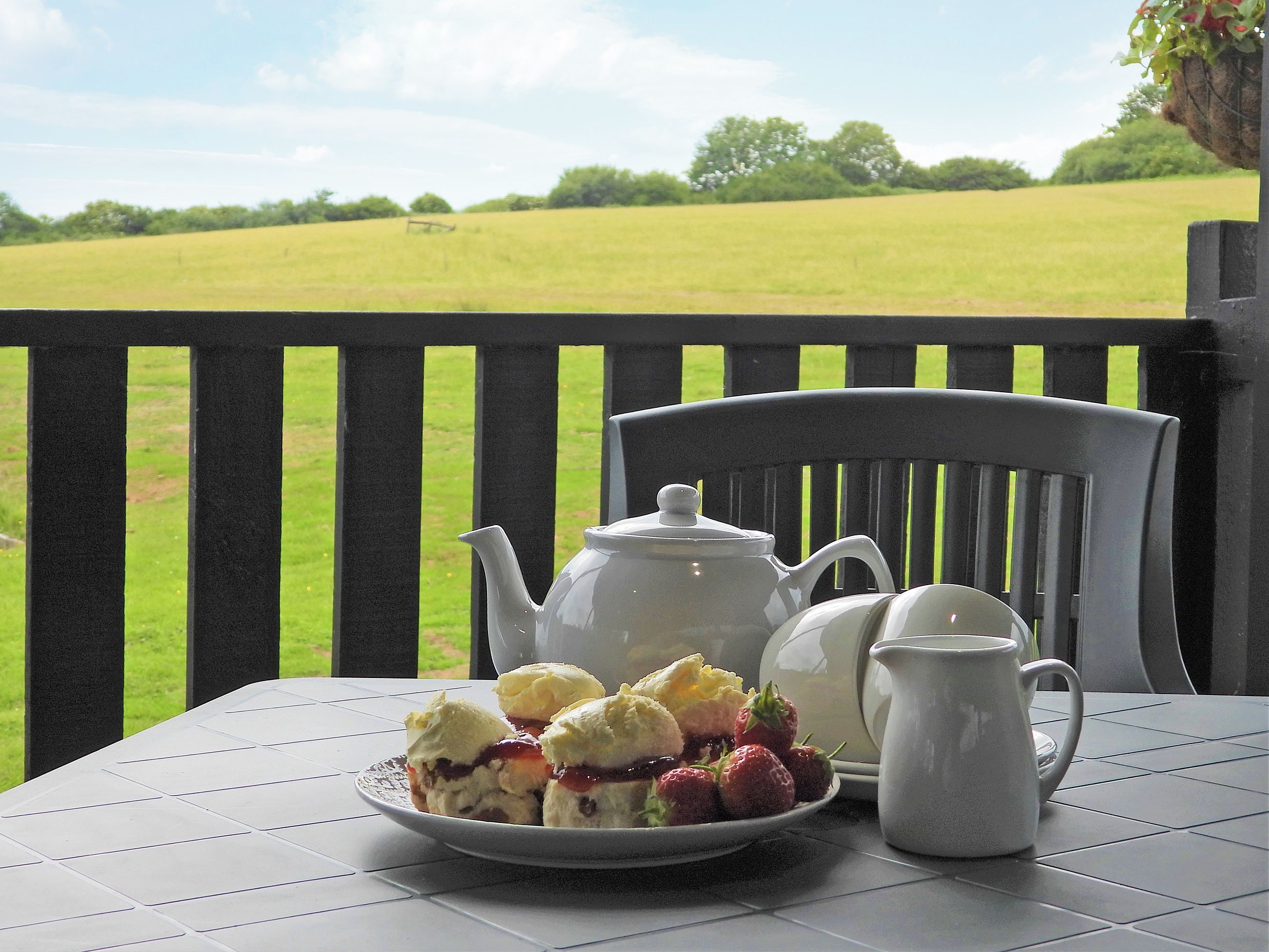 A table with a white teapot, a white jug, and a plate of scones with strawberries.