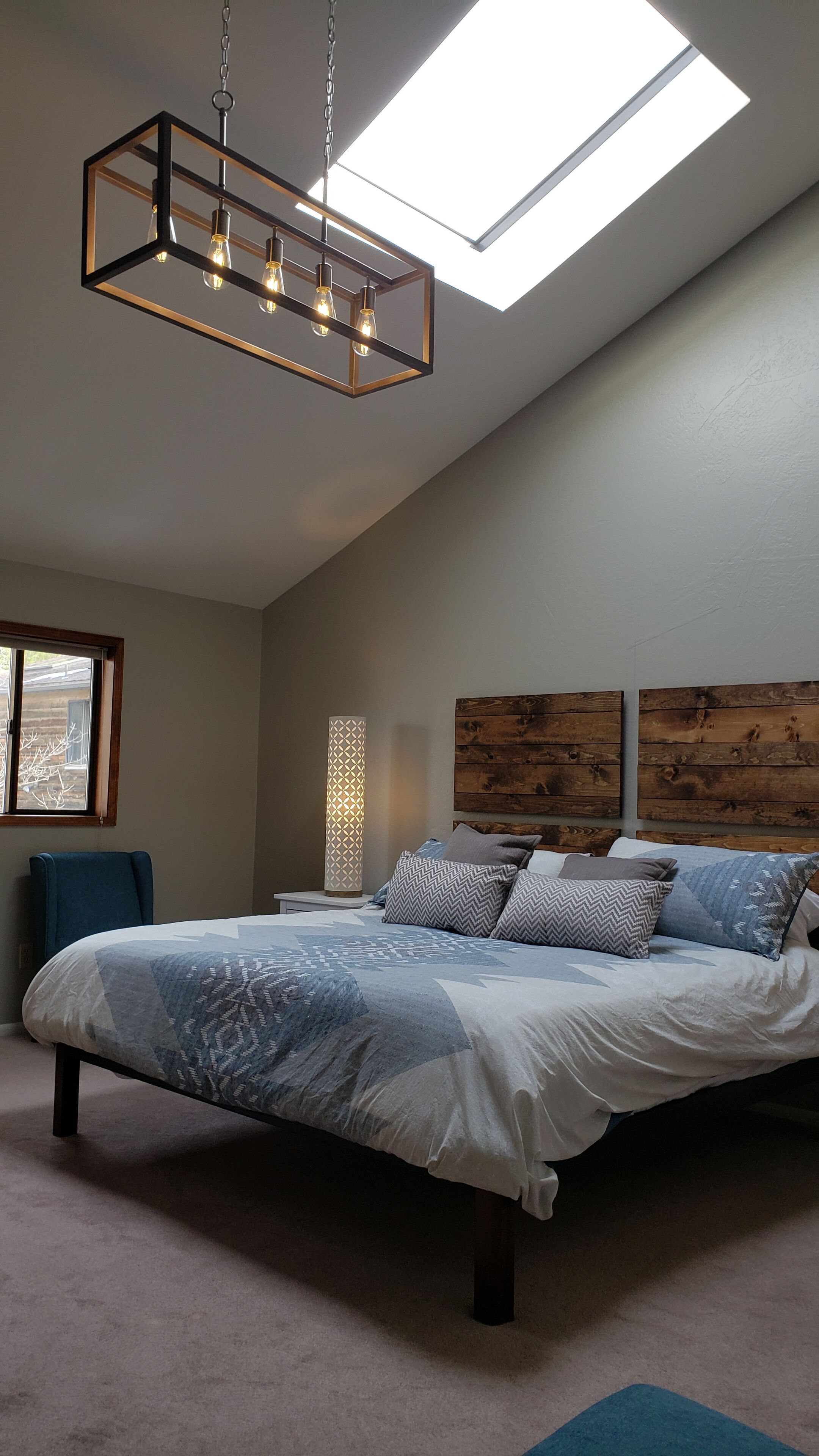 Une chambre à coucher avec un lit, une table de chevet, une lampe, une chaise et une lucarne.