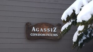 Ein Holzschild mit dem Schriftzug 'Agassiz Condominiums' an einer grauen Gebäudewand befestigt.