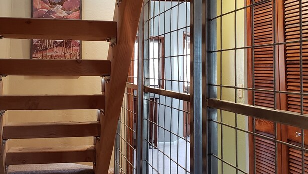 Eine Holztreppe mit Metallgeländern, Blick auf einen Raum mit Fenster und Tür, und ein Gemälde an der Wand.