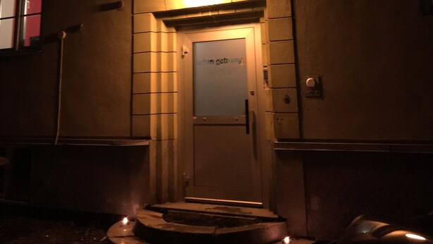 A building entrance with a lit sign above the door, steps leading up to it, and a window above the entrance. - Sleep And Go (Harnosand)