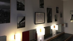 A hotel lobby with a long reception desk, framed photographs on the wall, and wall-mounted lighting. - Sleep And Go (Harnosand)