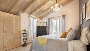 A bedroom with a bed, wooden ceiling beams, a dresser, and a window with curtains.