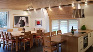A modern kitchen with wooden cabinetry, a dining area with wooden tables and chairs, and artwork on the walls.