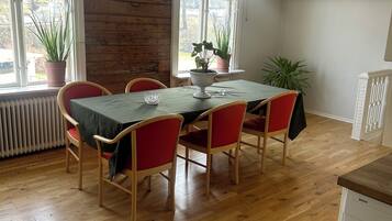 Uma área de refeições com mesa de madeira, cadeiras vermelhas, plantas em vasos e luminárias pendentes.