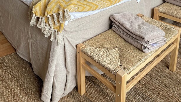 A bedroom with a bed, bedside tables, and a woven bench.